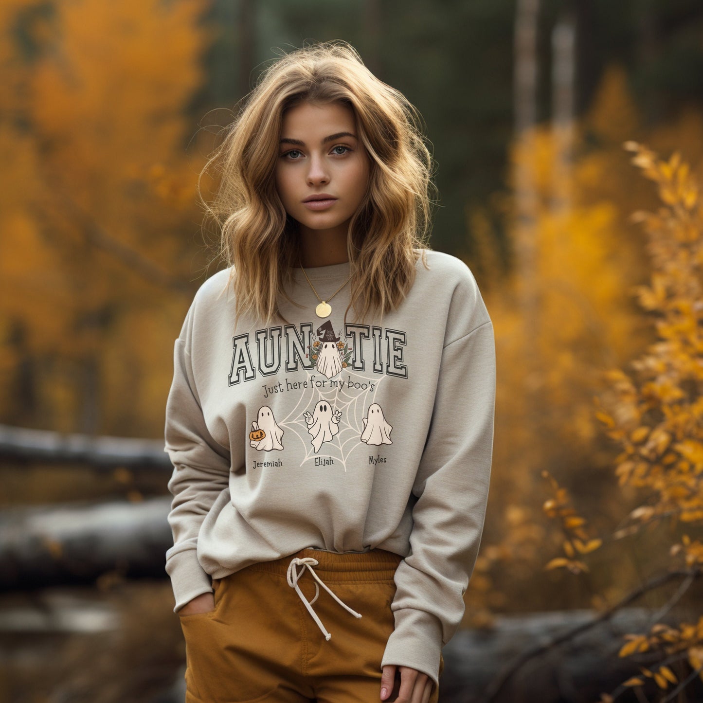 young woman wearing a sandstone color crewneck sweatshirt with Auntie and a ghost graphic that includes little ghost personalized with names under each one.